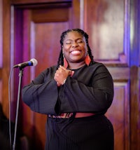 a woman in a black dress is standing in front of a microphone